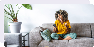 A woman excitedly scrolls on her phone while sitting on the couch.